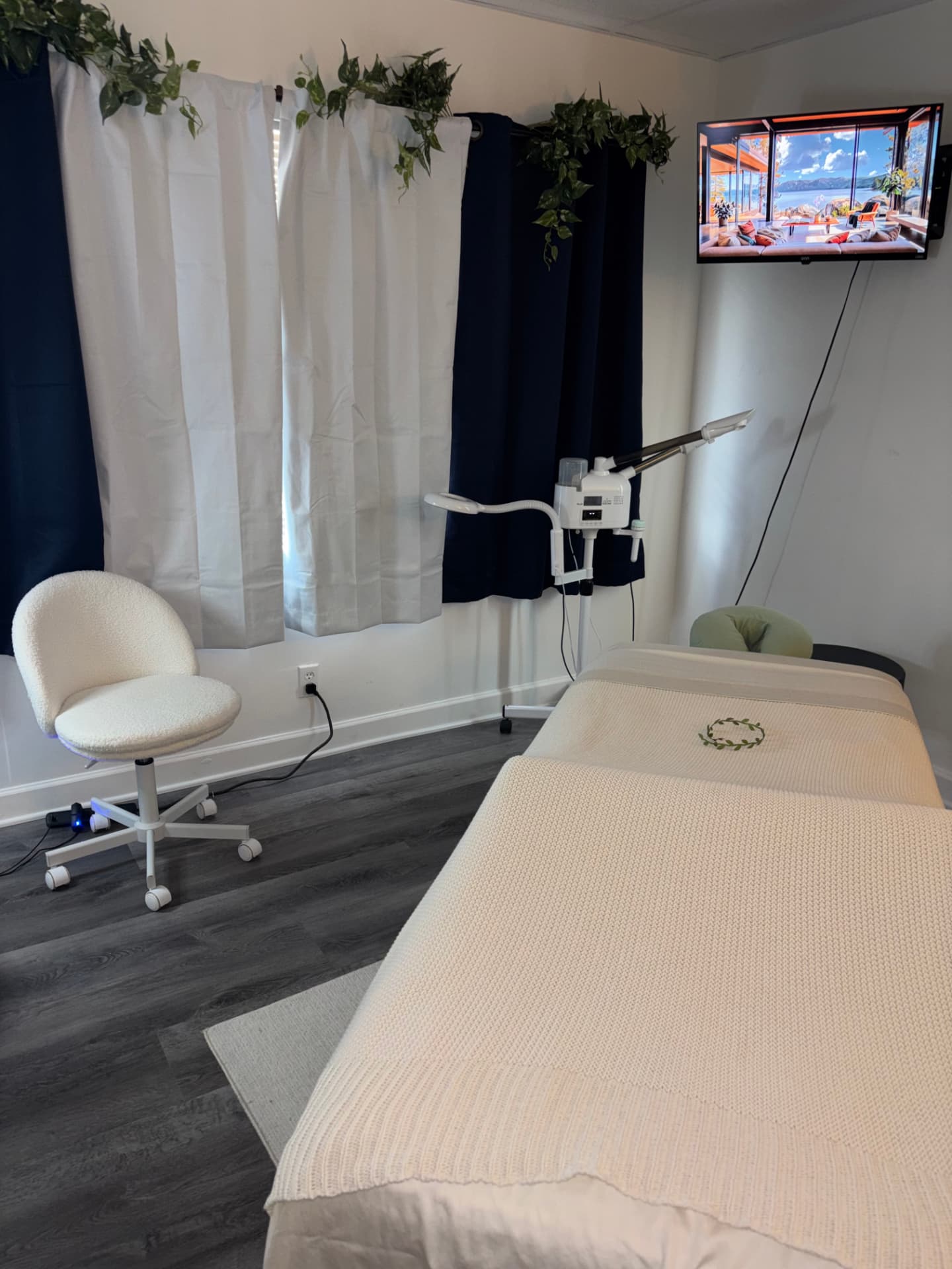 The Vital Bloom treatment room with a dressed massage table, facial steamer, and soft daylight through the curtains.